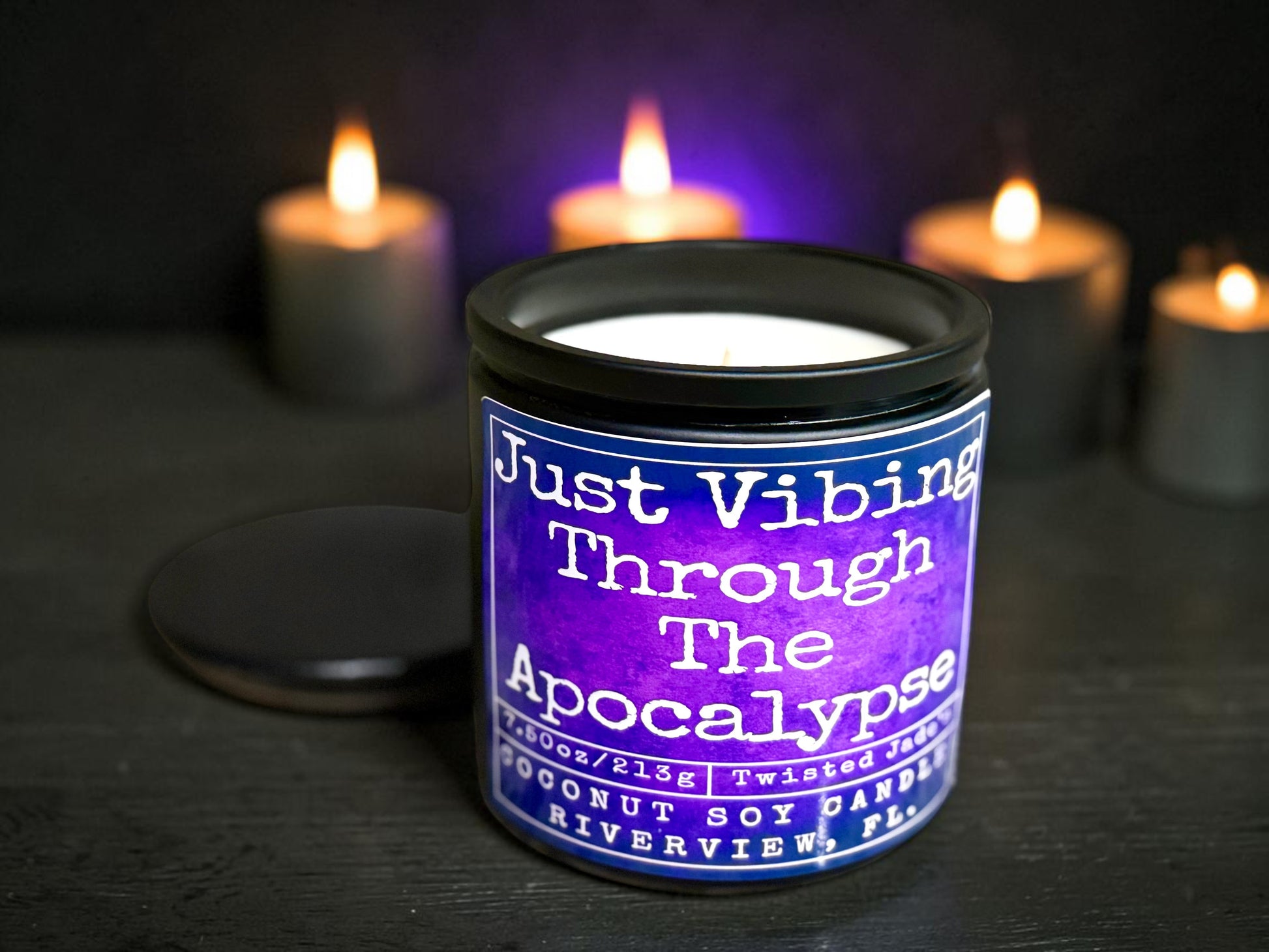 Twisted Jade's coconut soy candle with a purple label that reads "Just Vibing Through The Apocalypse."